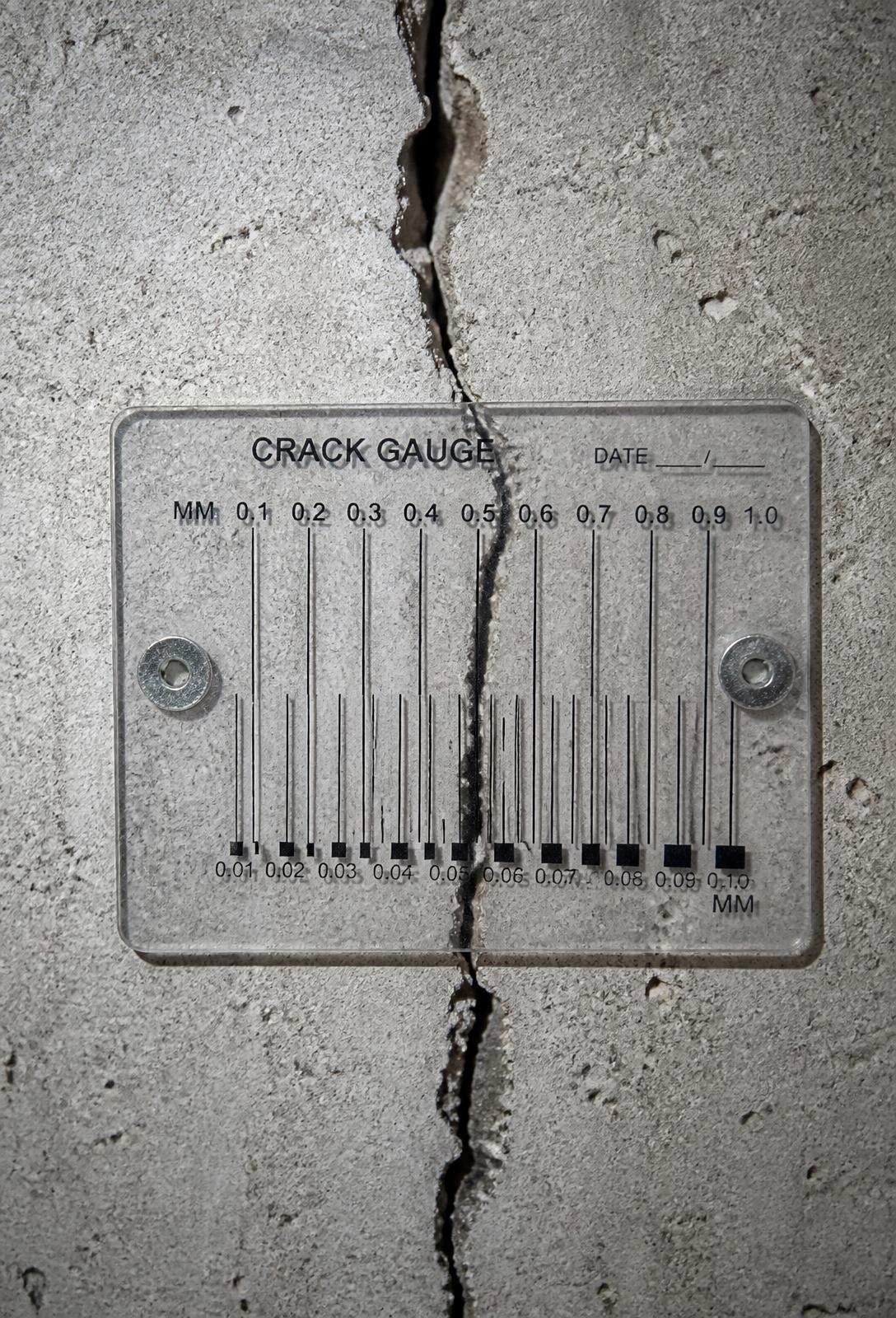 Crack gauge fixed across a structural crack in a concrete wall during inspection